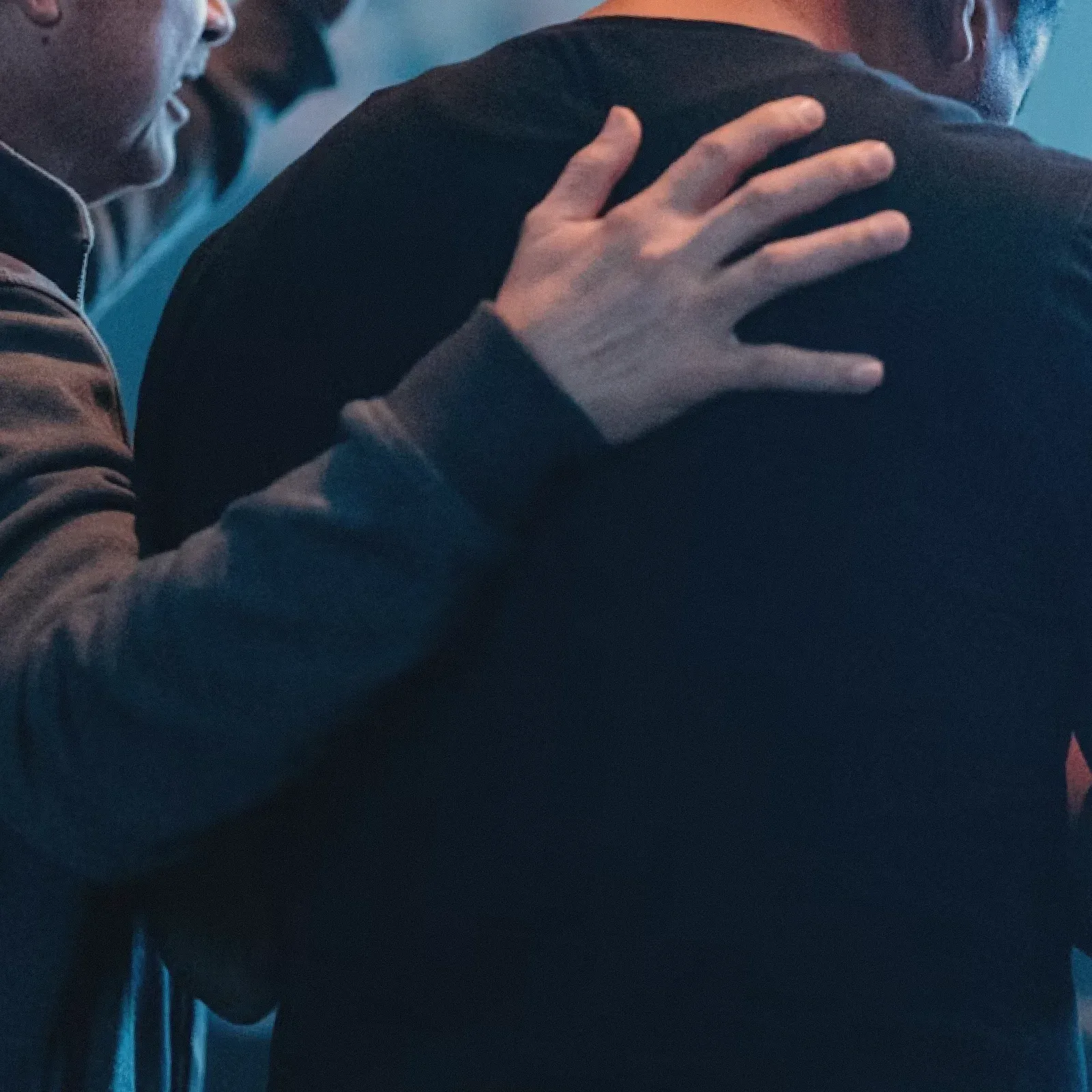 Eine Hand liegt betend auf der Schulter eines Menschen